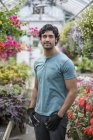 Young man standing in greenhouse full of flowering plants. — Stock Photo