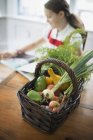 Basket of fresh farm vegetables with girl reading in kitchen. — Stock Photo