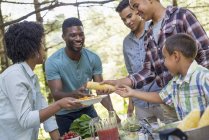 Adults and children standing around picnic table with food outdoors. — Stock Photo