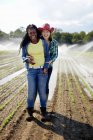 Two young women standing in field with irrigation sprinklers spraying seedlings. — Stock Photo