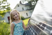 Elementary age girl posing beside solar panel in farmhouse garden. — Stock Photo