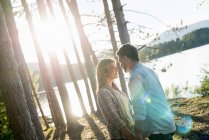 Couple standing face to face in woodland on shore of forest lake. — Stock Photo