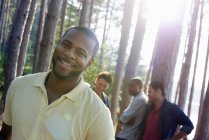 Hombre adulto sonriendo y mirando en cámara con amigos reunidos en pinos a orillas del lago . - foto de stock