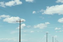 Poteaux téléphoniques, lignes électriques et ciel nuageux — Photo de stock