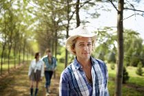 Молода людина в капелюсі ходить по сільській дорозі влітку з друзями на задньому плані . — стокове фото
