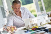 Mature man working on model of farmhouse at table in countryside. — Stock Photo