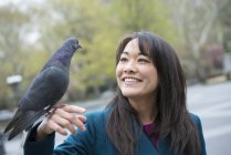 Young Asian woman holding perched pigeon on hand in city park. — Stock Photo