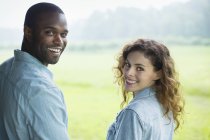 Young couple standing side by side in green field and looking over shoulders. — Stock Photo