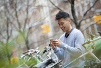 Чоловік в синьому светрі перевіряє смартфон за рядом припаркованих велосипедів . — стокове фото