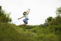 Pre-teen girl jumping in green meadow with arms outstretched. — Stock Photo