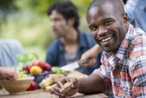 Mid adult man holding bread and smiling at outdoor party in garden. — Stock Photo