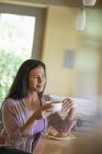 Молода жінка має чашку кави в кафе і дивиться вбік . — стокове фото