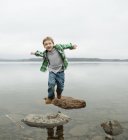 Elementary age boy jumping across stepping stones. — Stock Photo