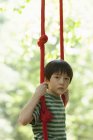 Elementary age boy sitting on swing outdoors. — Stock Photo