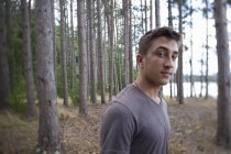 Junger Mann blickt in Kamera, während er im Wald steht. — Stockfoto