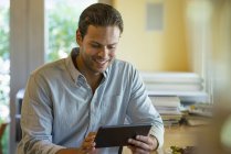 Homem sorrindo e usando tablet digital dentro de casa . — Fotografia de Stock