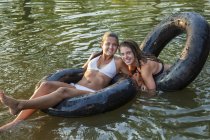 Dos chicas adolescentes flotando con flotadores de natación y neumáticos inflados . - foto de stock