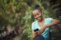 Chica adolescente sentada en el banco en el parque y utilizando el teléfono inteligente . - foto de stock
