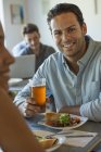 Man smiling and looking in camera at cafe table with glass of beer. — Stock Photo