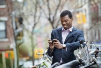 Young man in blue suit checking smartphone in bicycle park. — Stock Photo
