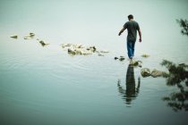 Man walking barefoot across stepping stones away from shore of lake. — Stock Photo