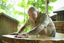 Зрілий чоловік полірує зовнішні дерев'яні меблі в сільській місцевості — стокове фото