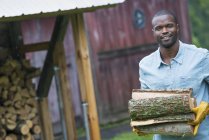 Young man carrying pile of logs from the store at farm. — Stock Photo