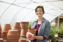 Femme portant des gants de travail portant des pots de plantes en terre cuite en serre . — Photo de stock