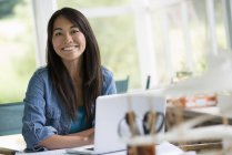 Femme au bureau travaillant à l'ordinateur portable, souriant et regardant à la caméra . — Photo de stock