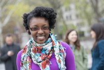 Young woman with floral scarf smiling and looking in camera with people in background. — Stock Photo