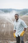 Jovem agricultor em roupas de trabalho em campo orgânico com irrigação de aspersores de água . — Fotografia de Stock