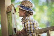 Blond boy in hat leaning on porch with bug box. — Stock Photo
