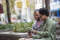Couple sitting side by side on bench and looking at phone. — Stock Photo