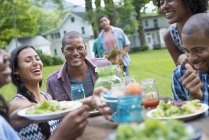 Giovani amici che condividono i piatti con il cibo al tavolo da picnic nel giardino di campagna . — Foto stock