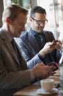 Businessmen sitting at cafe table and checking mobile phones. — Stock Photo