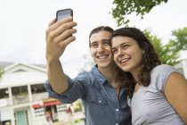 Giovane coppia in piedi fianco a fianco e prendendo selfie sulla strada . — Foto stock