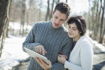 Jovem casal olhando para tablet digital na floresta no inverno . — Fotografia de Stock