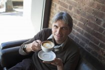 Homem sentado no café e segurando xícara de cappuccino espumoso . — Fotografia de Stock
