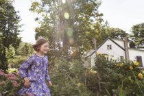 Kind in gemustertem blauem Kleid läuft durch Hausgarten. — Stockfoto