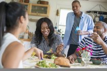 Group of friends laughing and sharing dinner in country kitchen interior. — Stock Photo