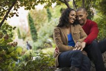 Mid adult couple sitting close together under trees in city park. — Stock Photo