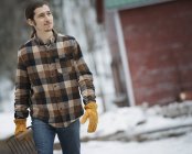 Man in plaid shirt walking across snow-covered ground with pitchfork. — Stock Photo