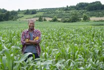 Молодий чоловік з обіймами схрестив стоячи на полі кукурудзи на органічній фермі . — стокове фото