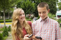 Teenage boy and girl smiling and holding smartphones on street. — Stock Photo
