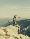 Male hiker sitting on rocks and holding smartphone on summit of Surprise Mountain, Mount Baker National Forest, Washington, USA. — Stock Photo