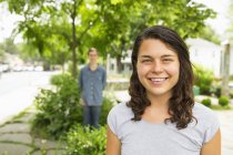 Молодая женщина стоит на улице с молодым человеком, стоящим на заднем плане — стоковое фото
