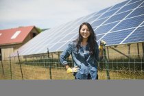 Mujer joven apoyada en la cerca frente al panel solar en la granja en el campo . - foto de stock