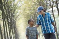 Young man and elementary age boy walking down avenue of trees. — Stock Photo