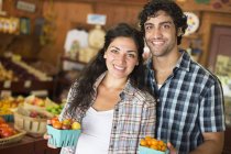 Jeune homme et jeune femme posant ensemble avec des conteneurs de tomates mûres dans un magasin d'agriculteurs biologiques
. — Photo de stock