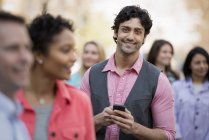 Jeune homme tenant un téléphone portable parmi un groupe d'hommes et de femmes . — Photo de stock